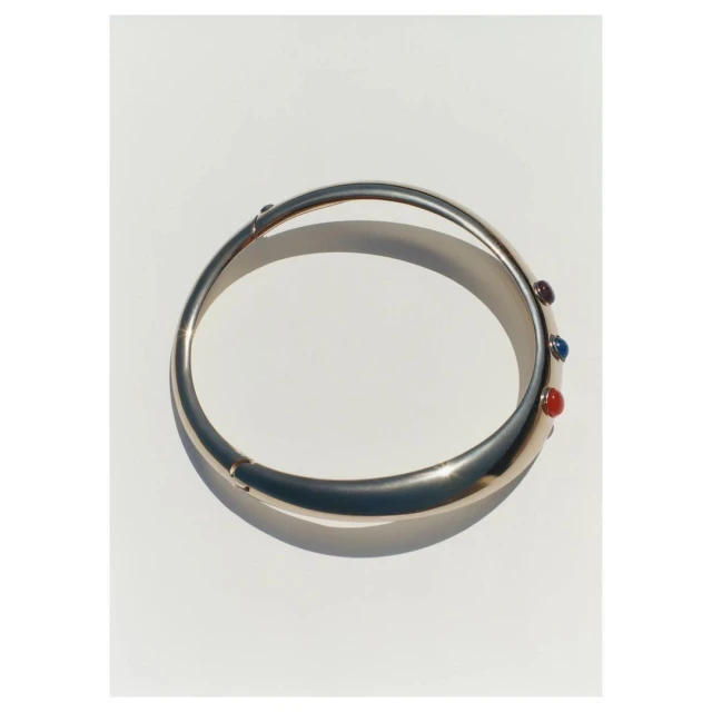 Gold bangle bracelet with red, purple and blue stones accents displayed on a white surface. Jewellery photography.