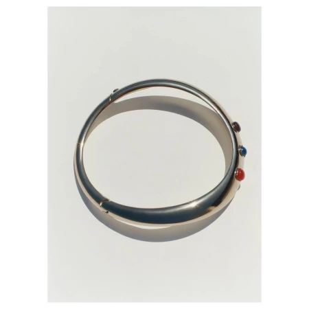Gold bangle bracelet with red, purple and blue stones accents displayed on a white surface. Jewellery photography.