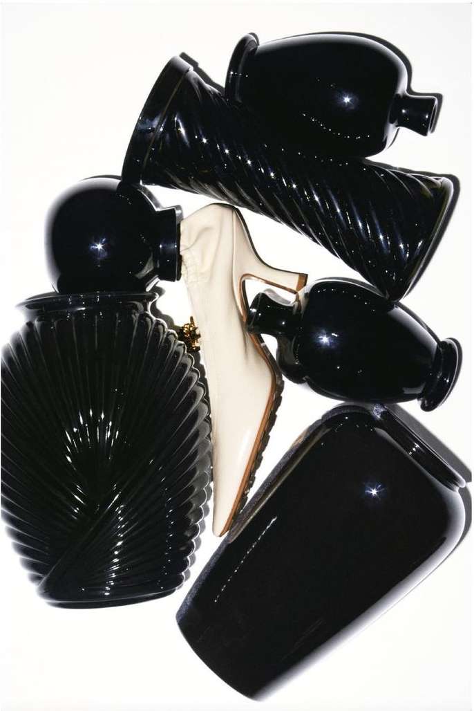 Arrangement of black vases with varied shapes and textures alongside a single white high heel shoe on a white background.