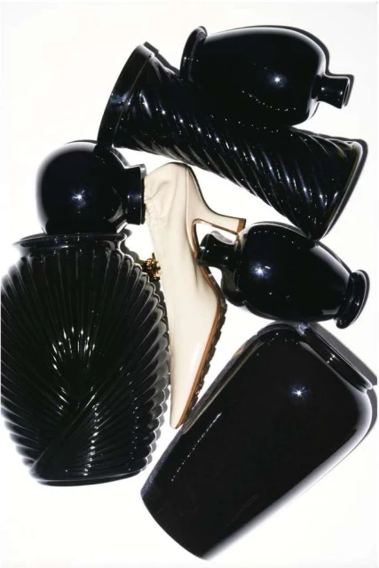 Arrangement of black vases with varied shapes and textures alongside a single white high heel shoe on a white background.