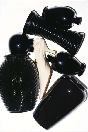 Arrangement of black vases with varied shapes and textures alongside a single white high heel shoe on a white background.