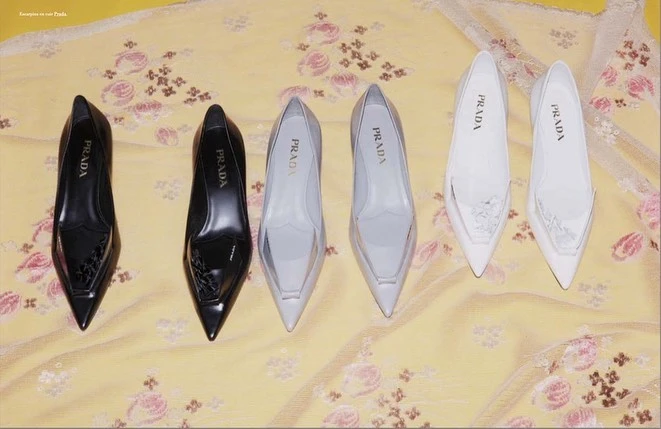 Three pairs of pointed-toe Prada leather pumps in black, grey, and white arranged on yellow floral fabric.