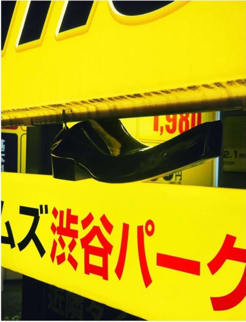 Black heeled shoe rests on a yellow sign featuring red Japanese lettering and numbers, under bright lighting.