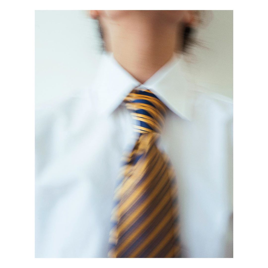 A blurred medium shot of a person wearing a white dress shirt and a blue and gold striped tie, focusing on the shirt and tie details.