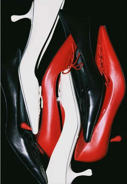 Multiple pairs of red, black, and white leather high heel shoes on a black background, with a focus on texture and form.
