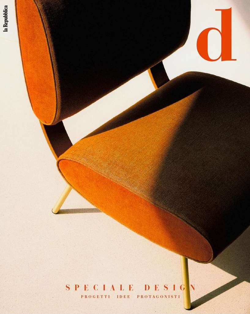 An orange and dark brown modern chair in a studio setting with soft lighting, showcasing furniture design against a cream backdrop.