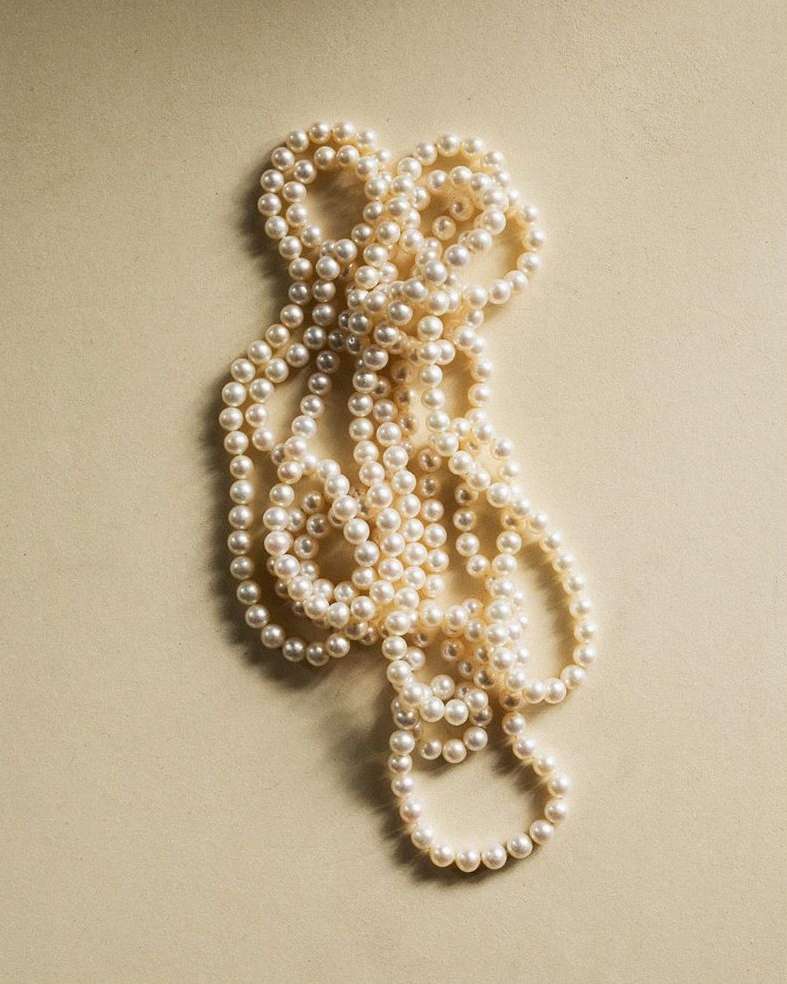 Strand of cream-colored pearls on a beige background, close-up studio shot. Elegant jewelry accessory for fashion or beauty.