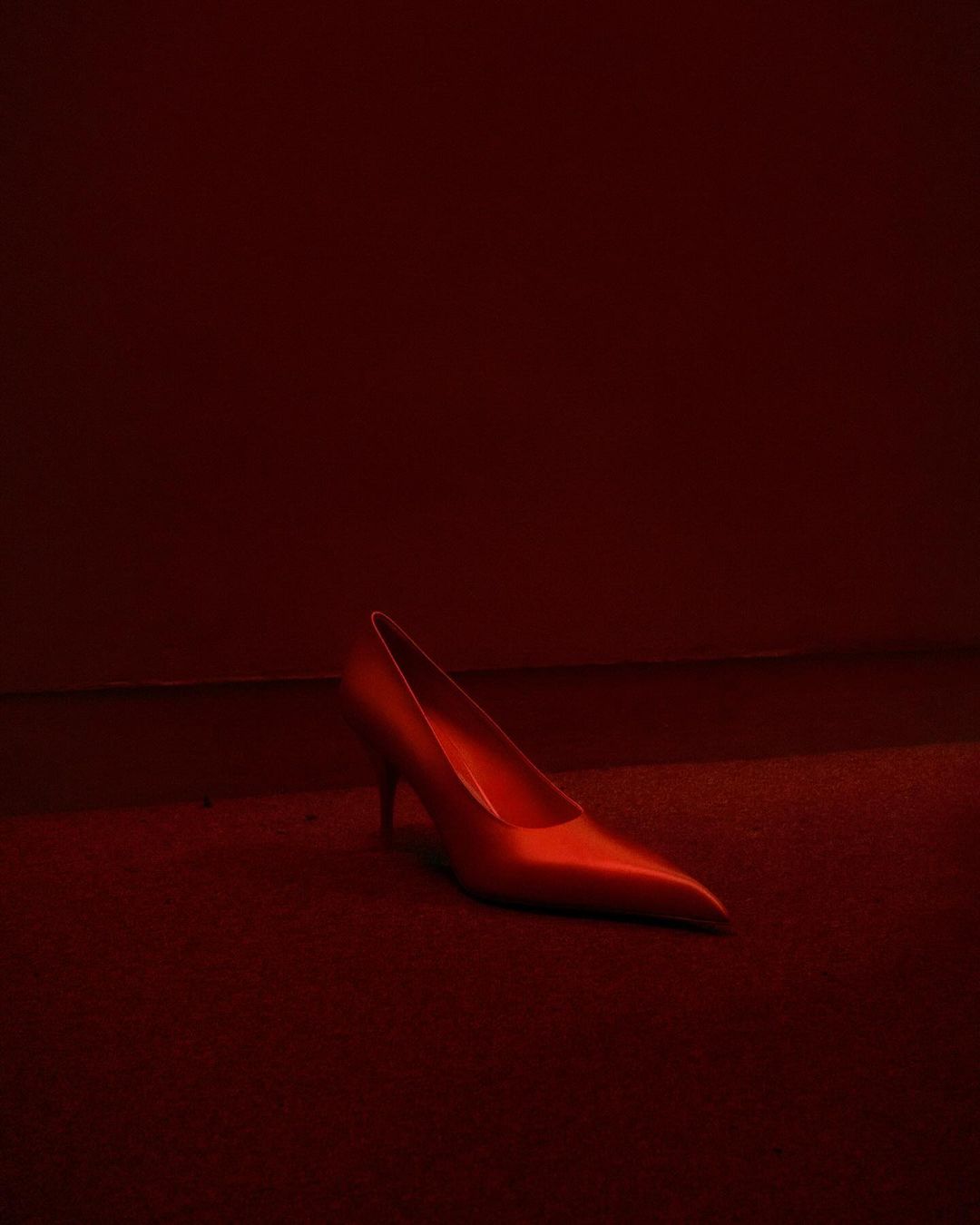 Elegant red stiletto heel rests on matching red carpet in a dimly lit space, creating a dramatic and monochromatic fashion statement.