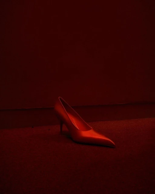 Elegant red stiletto heel rests on matching red carpet in a dimly lit space, creating a dramatic and monochromatic fashion statement.