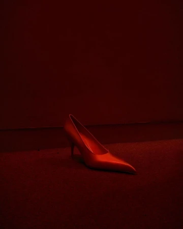 Elegant red stiletto heel rests on matching red carpet in a dimly lit space, creating a dramatic and monochromatic fashion statement.