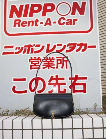 Elegant black YSL purse rests on a tiled wall, set against a sign with Japanese text and a logo. The bag is sleek and modern.