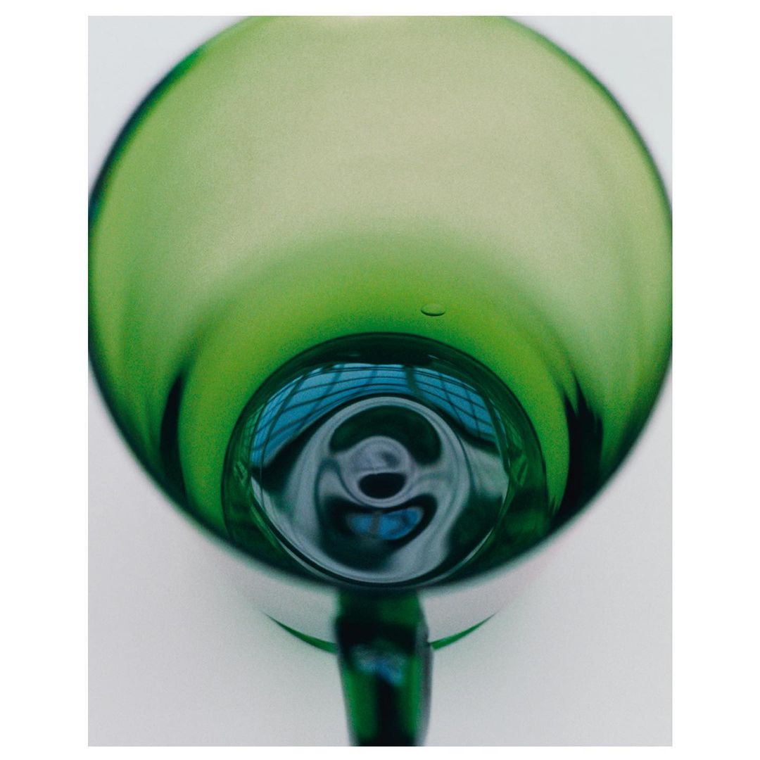 Abstract close-up of a green glass mug, showcasing its rounded shape, reflective surfaces, and the light passing through it. 