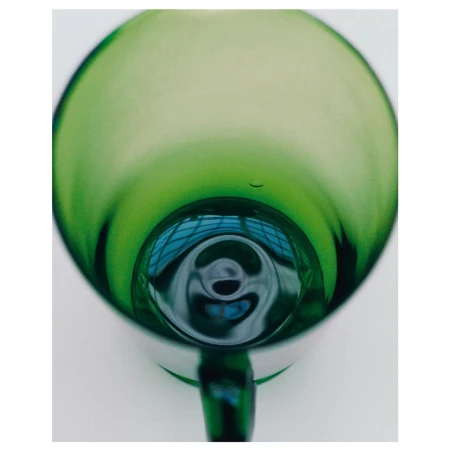 Abstract close-up of a green glass mug, showcasing its rounded shape, reflective surfaces, and the light passing through it. 