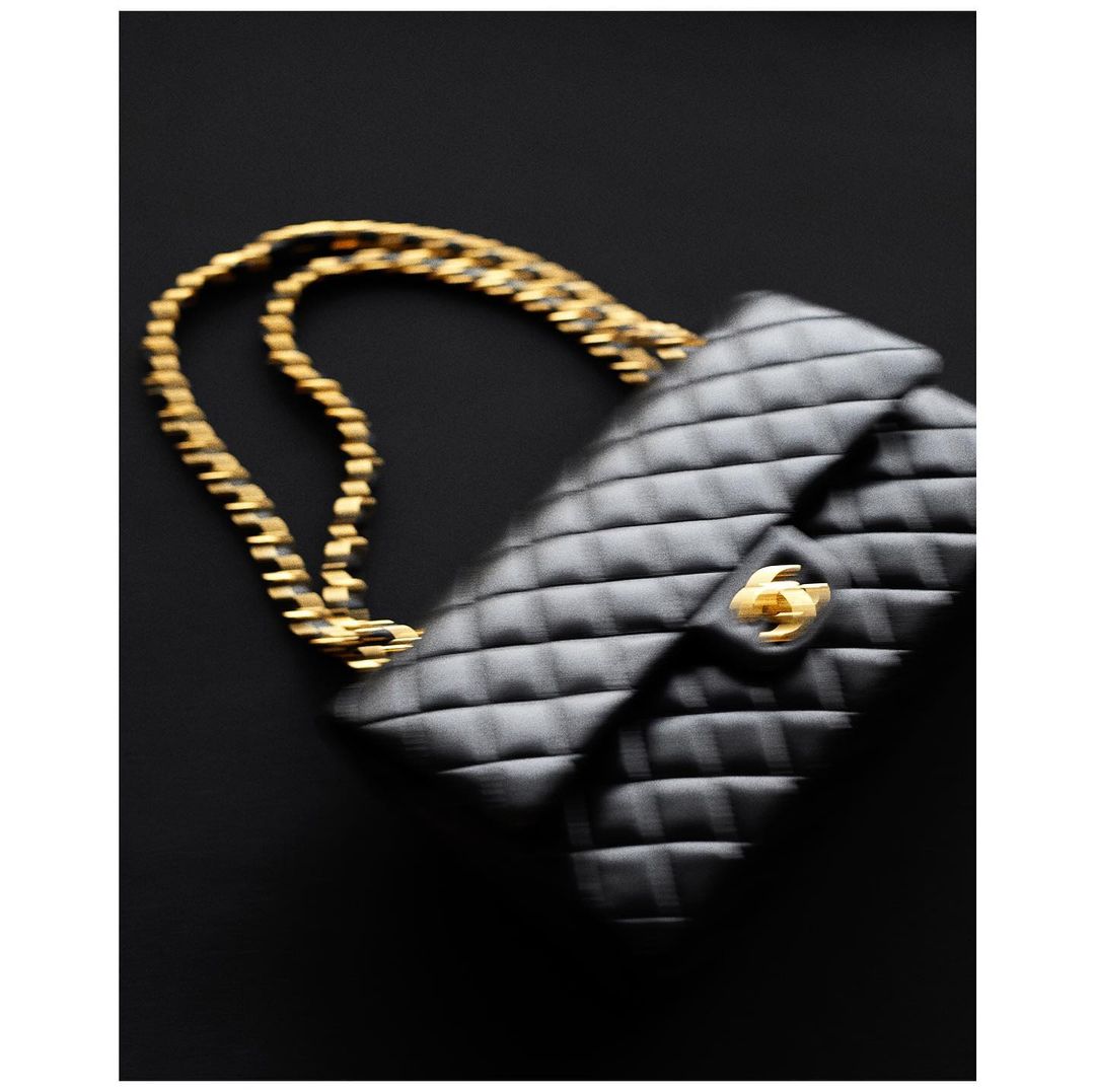 Elegant black quilted leather handbag with a golden chain strap and closure detail, displayed against a dark, contrasting background.