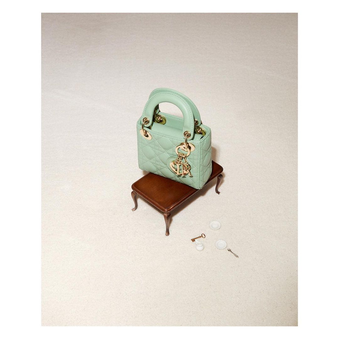 Mint green Lady Dior mini handbag on a tiny brown wooden table, studio shot. Gold logo charms add elegance to this luxury fashion accessory.