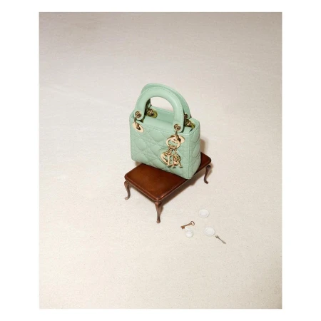 Mint green Lady Dior mini handbag on a tiny brown wooden table, studio shot. Gold logo charms add elegance to this luxury fashion accessory.