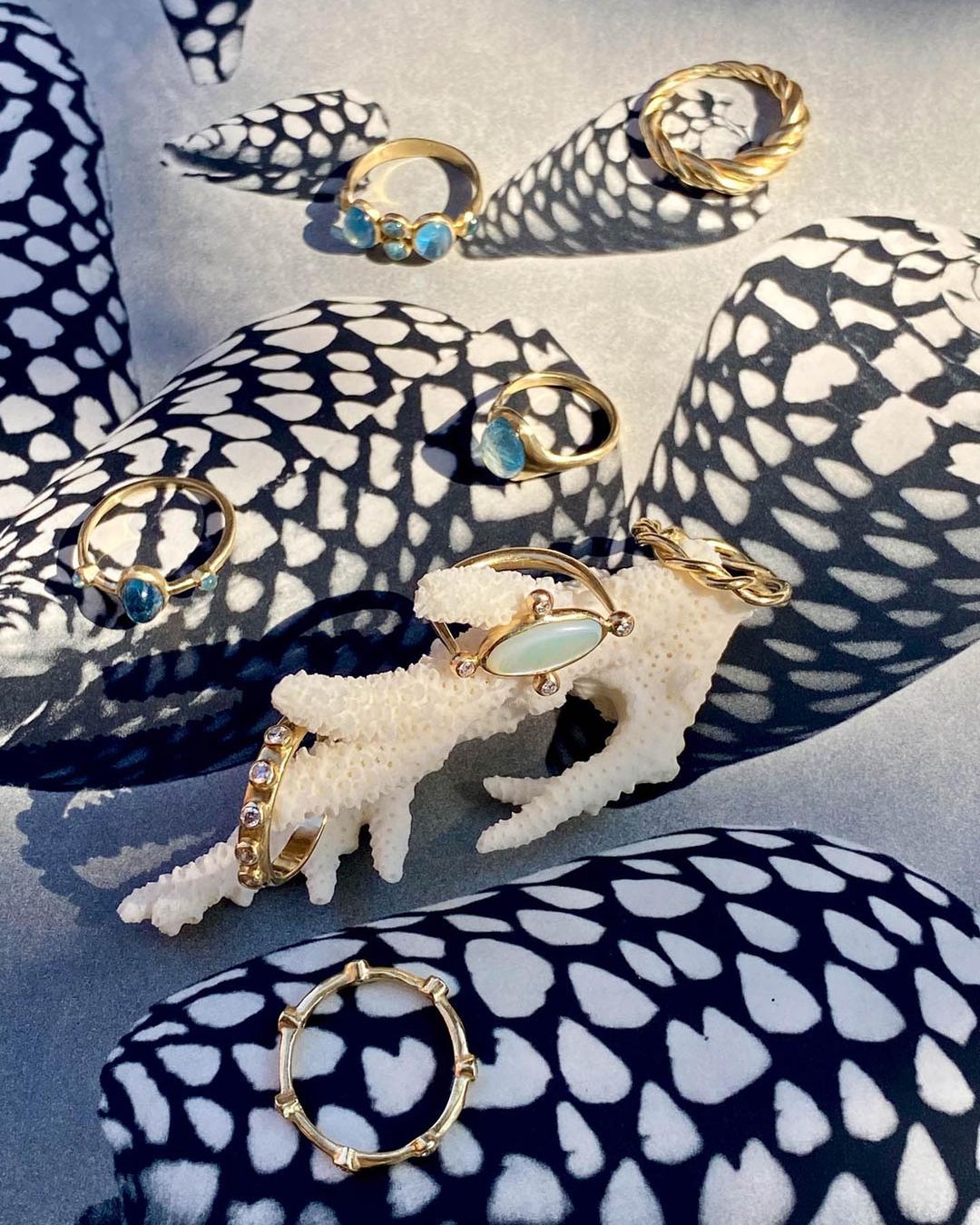 Elevated shot of gold rings with gemstones displayed on coral on a patterned surface with shadows, jewelry photography for retail.