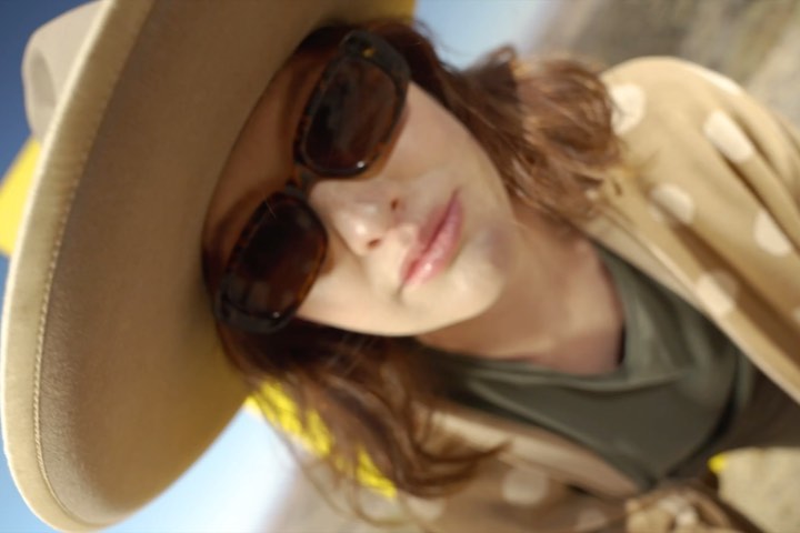 Woman wearing sunglasses and wide-brimmed hat poses outdoors, showcasing fashion accessories in a close-up, angled shot with soft natural light.
