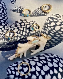 Several gold rings with blue and white stones resting on white coral and patterned surfaces by Joaquin Trujillo.