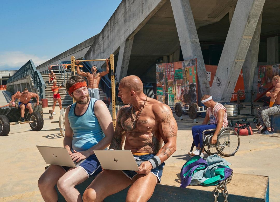 A group of men at an outdoor gym work on laptops and lift weights. A sunny day with an urban environment and HP laptops.