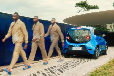 Motion blur photograph of a man walking past a parked bright blue electric car on a paved path in Düsseldorf by Jochen Manz
