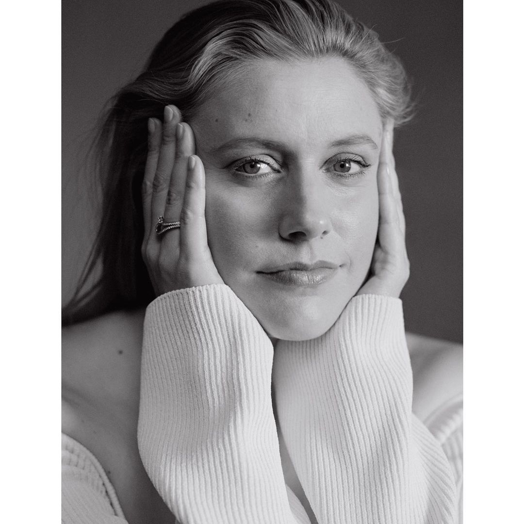 Black and white portrait of an adult female with her hands near her face, wearing a textured, light-colored sweater against a neutral backdrop.
