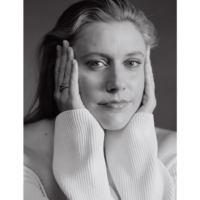 Black and white portrait of an adult female with her hands near her face, wearing a textured, light-colored sweater against a neutral backdrop.