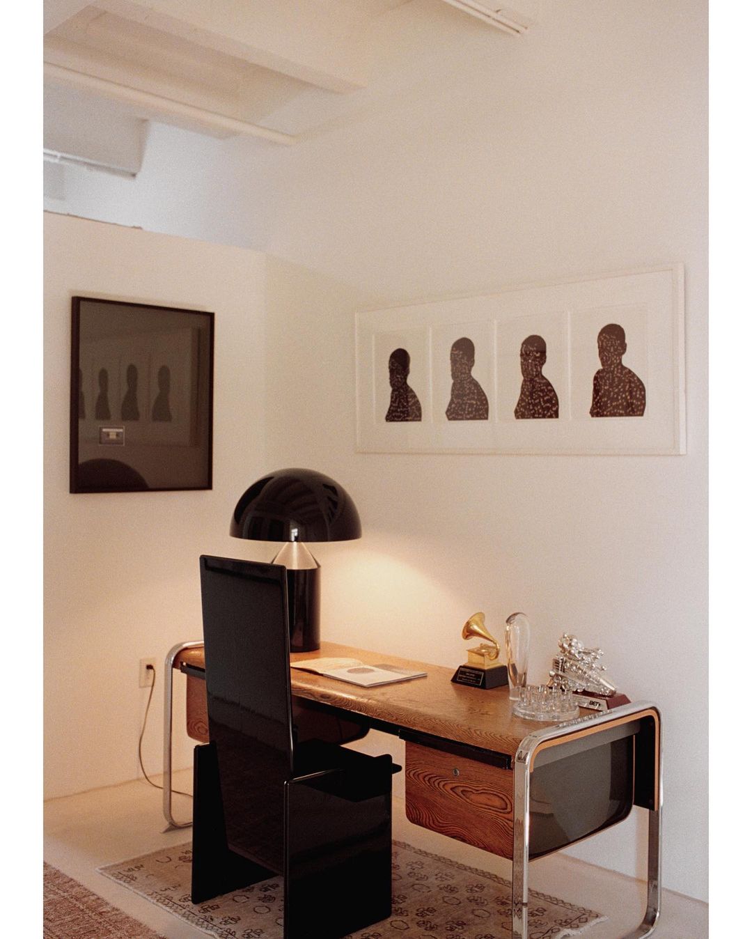 Home office area featuring a wooden desk with black chair, framed art on the wall, and decor in a brightly lit interior space.
