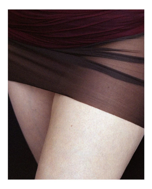 Close-up of a human's crossed legs and thighs covered with sheer black fabric on a dark background, illuminated with soft lighting.