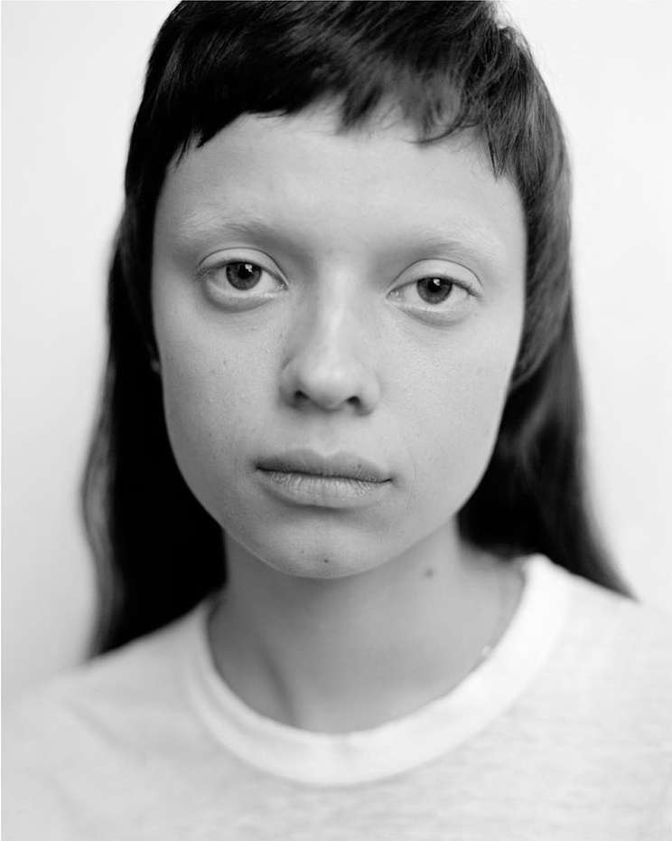 Monochrome portrait of a woman with short bangs wearing a t-shirt, captured in a photo studio against a plain background.