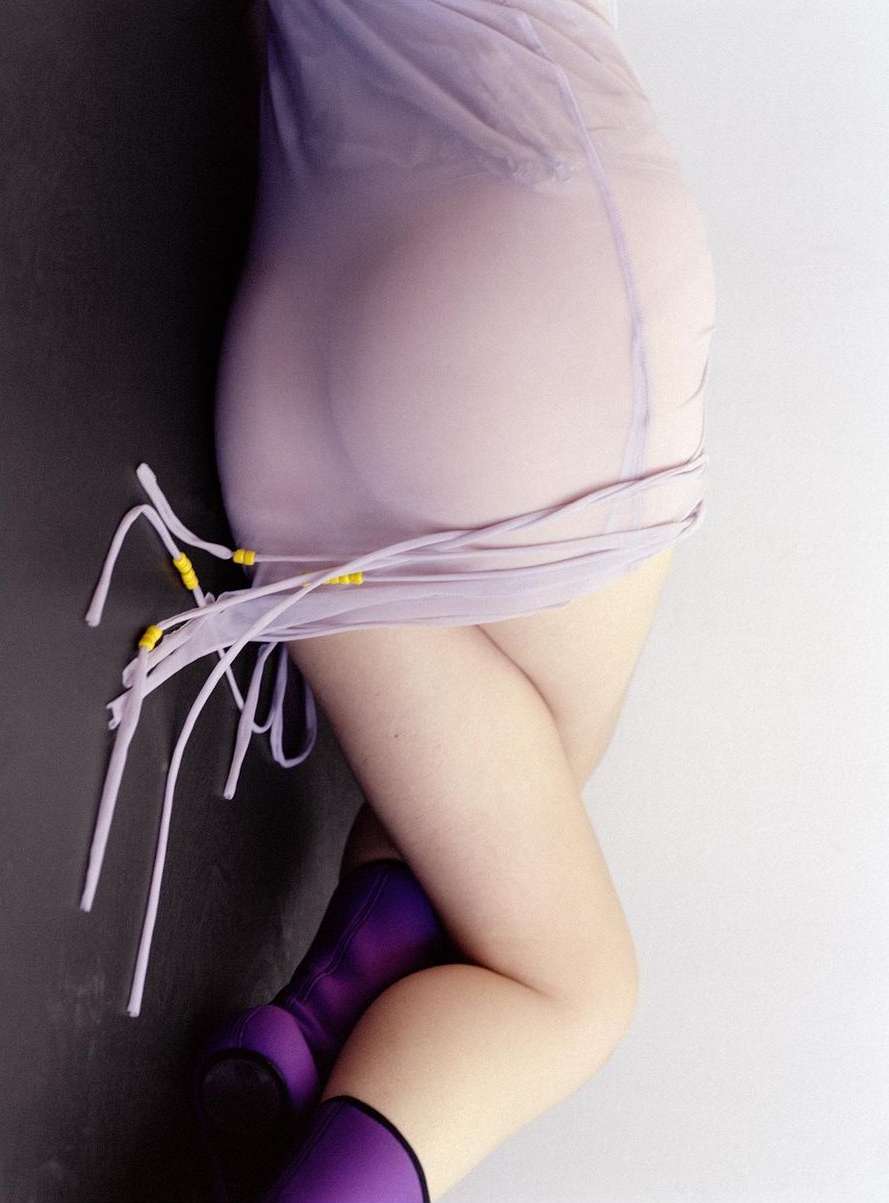 Torso and legs of a woman in a semi-sheer lilac dress and purple boots posing against a split black and white background.