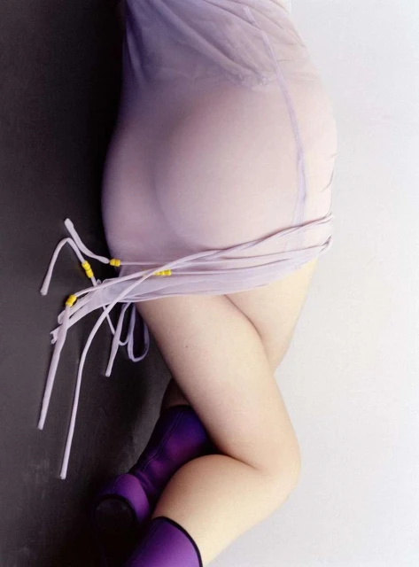 Torso and legs of a woman in a semi-sheer lilac dress and purple boots posing against a split black and white background.