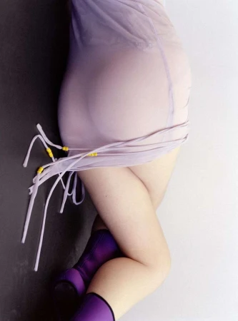 Torso and legs of a woman in a semi-sheer lilac dress and purple boots posing against a split black and white background.
