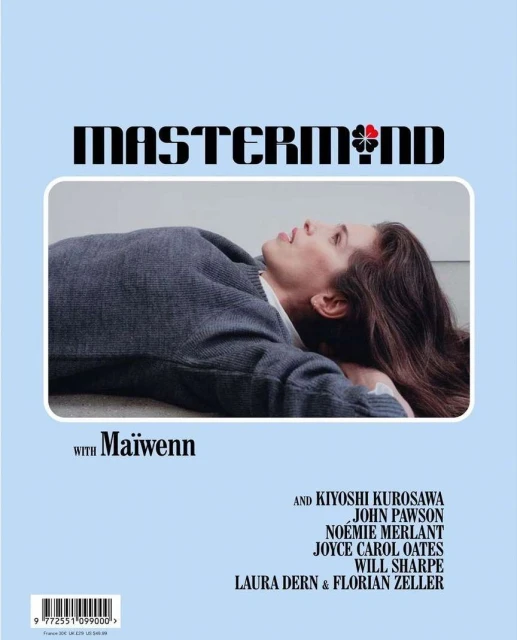 Woman lying down wearing a grey sweater, photographed in a studio with light blue background and MASTERMIND brand text above her.