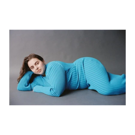 A woman wearing a ribbed bright blue matching top and pants lying on a grey seamless studio floor.