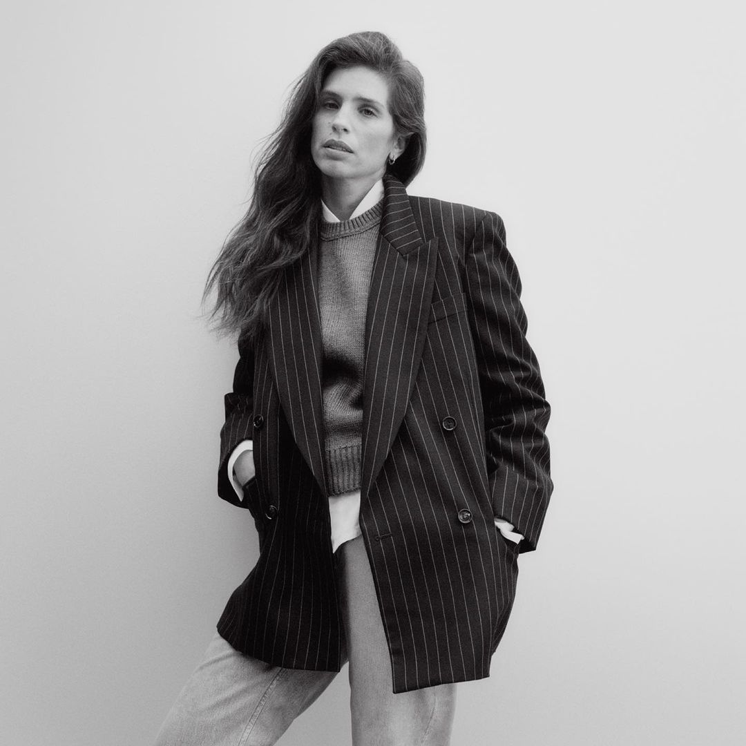 Portrait of a woman wearing a pinstripe blazer and knit sweater against a plain white background by Jody Rogac.