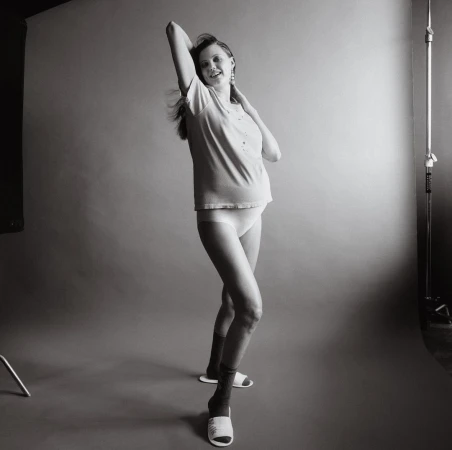 Pregnant woman in t-shirt and underwear posing in a studio with grey seamless backdrop, photographed by Jody Rogac.