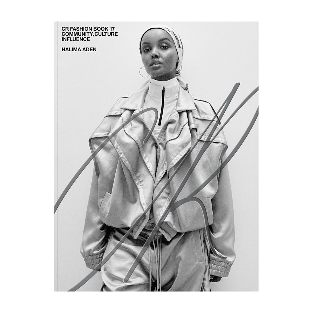 Black and white fashion shot of Halima Aden in an oversized jacket and head covering for CR Fashion Book. Studio setting, neutral backdrop.