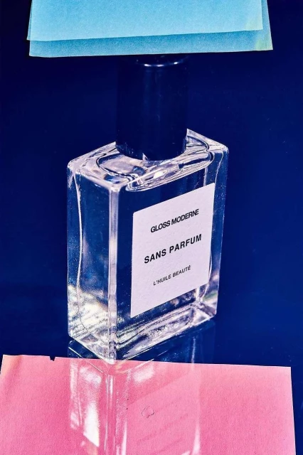 Product shot of a clear glass perfume bottle with a black cap against a deep blue background with colored paper accents.