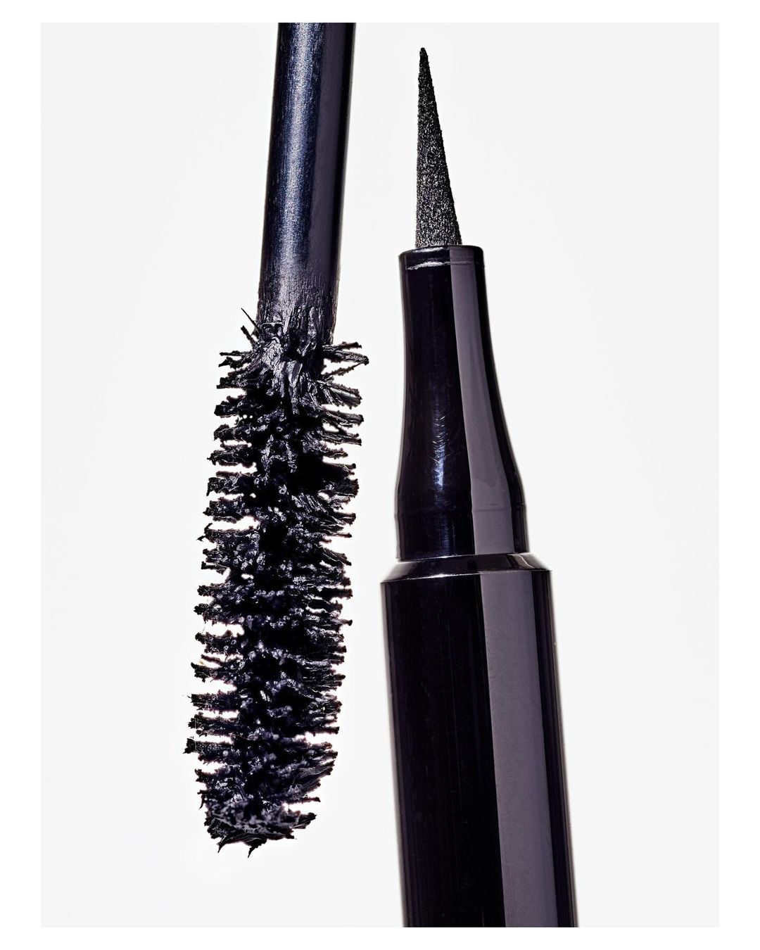 Close-up shot of black eyeliner and mascara wands with synthetic bristles against a bright white backdrop, beauty product display.