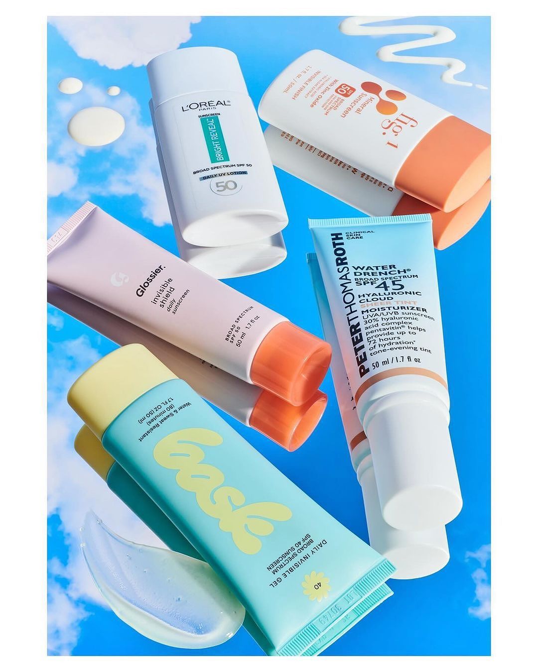 Display of sunscreen tubes and bottles from various brands, set against a sky-blue background with cloud accents.