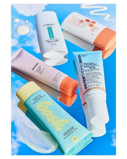 Display of sunscreen tubes and bottles from various brands, set against a sky-blue background with cloud accents.