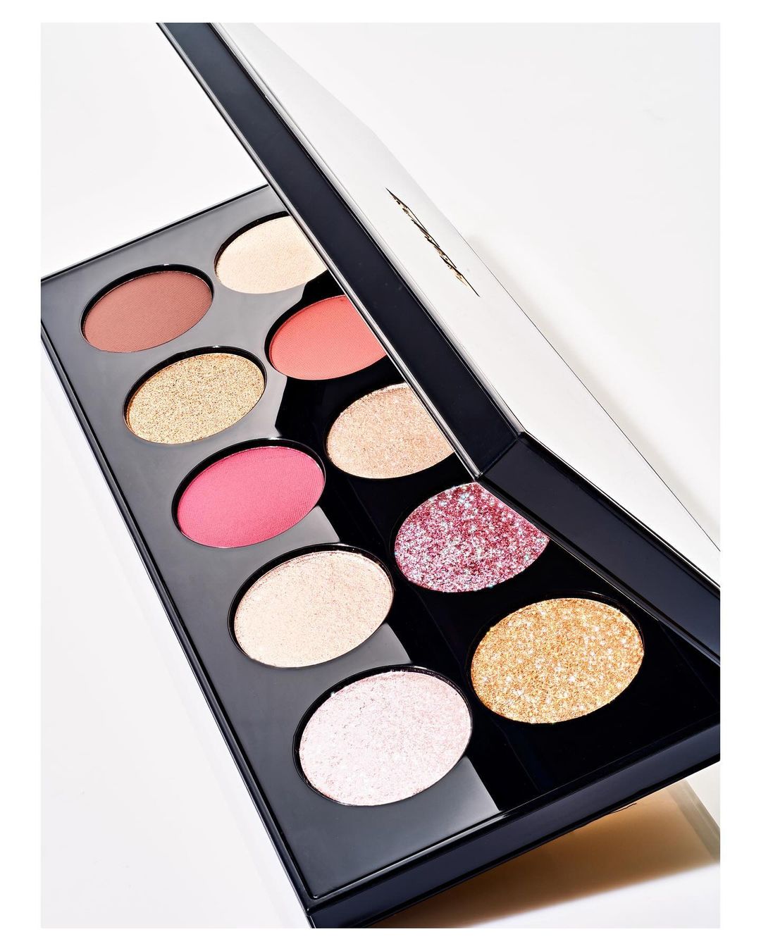 Eye shadow palette featuring a variety of colors including pink, gold, and bronze hues with a glossy black case and white background.
