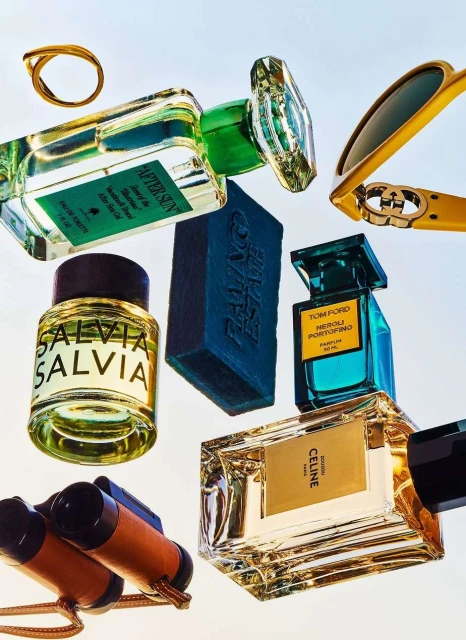 Still life featuring perfume bottles from Tom Ford, Celine, and other luxury brands, along with sunglasses, soap, a ring, and binoculars.