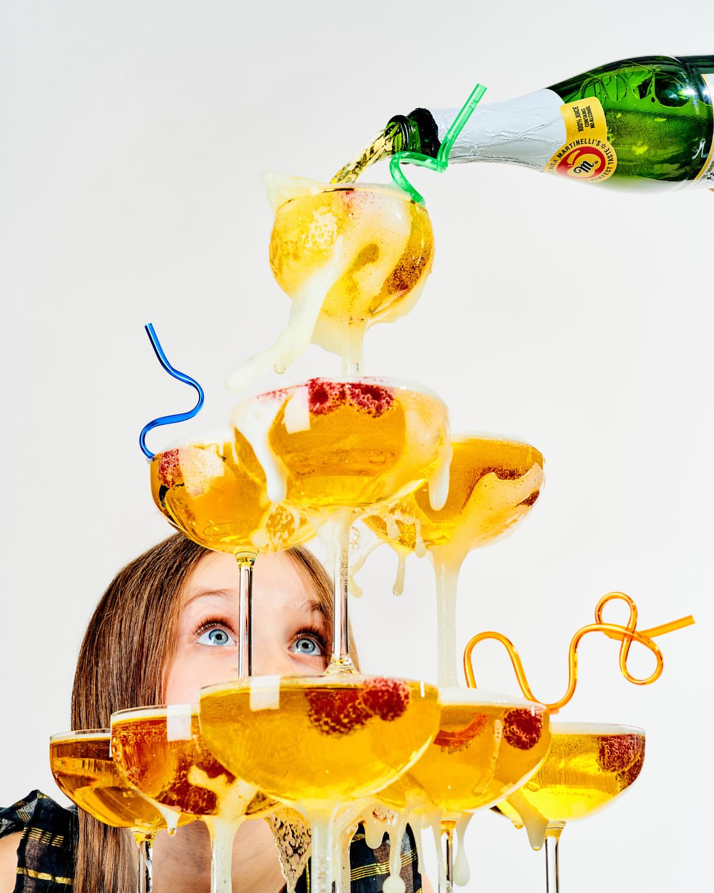 Champagne tower celebration with an adult female peeking between the glasses and a bottle of champagne pouring into the tower.
