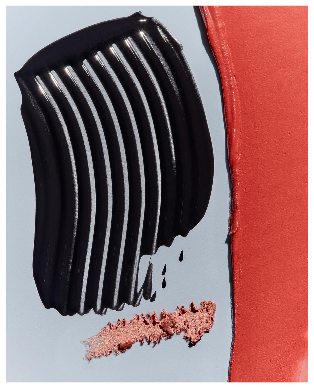 Close-up of smears of cosmetic products in black and coral tones on a light-blue surface. Visual showcase of beauty products.