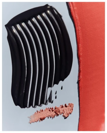 Close-up of smears of cosmetic products in black and coral tones on a light-blue surface. Visual showcase of beauty products.