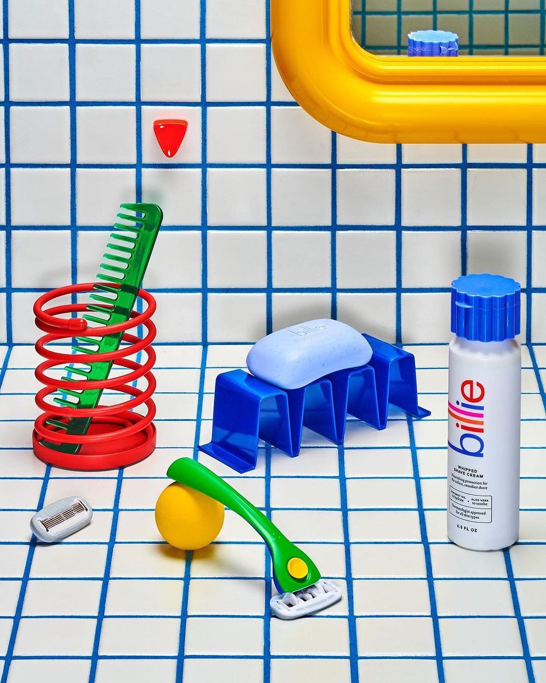 Still life of bathroom objects including soap, razor, comb, bottle, and holder arranged on a tiled surface with blue lines.