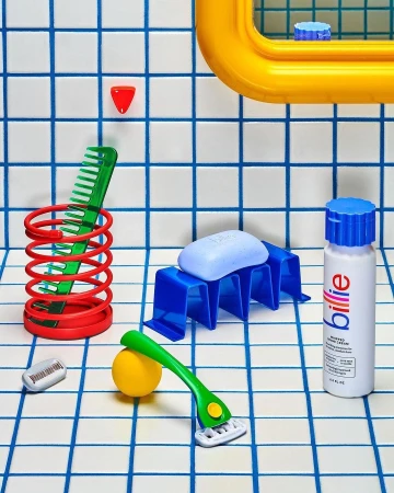 Still life of bathroom objects including soap, razor, comb, bottle, and holder arranged on a tiled surface with blue lines.