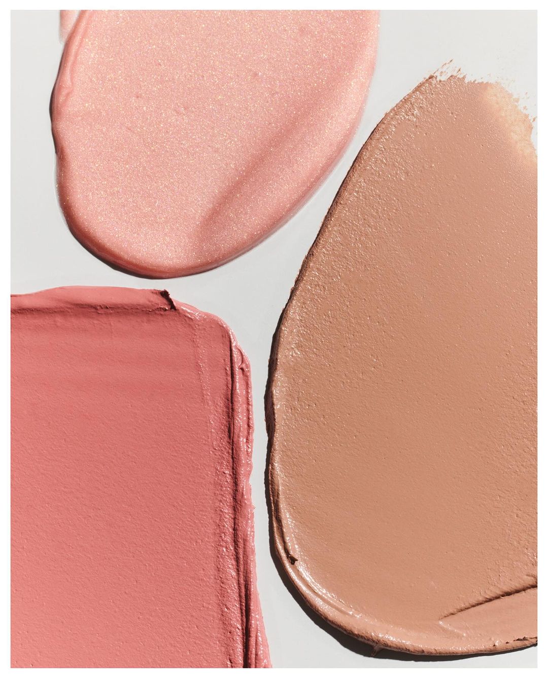 Close-up of three cream makeup swatches in pink and tan hues against a white background, suitable for beauty and cosmetics promotions.